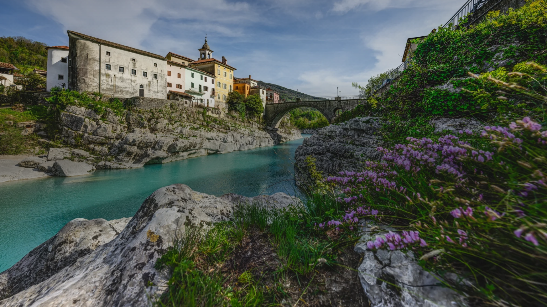 Panoramska fotografija Kanala ob Soči z mostom čez smaragdno zeleno reko Sočo.